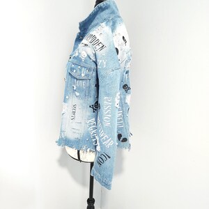 Puede incluir: Chaqueta vaquera azul claro con detalles desgastados, con estampados negros de calaveras y huesos cruzados, corazones y textos, incluyendo "Forbidden", "Love", "Secrets", "Passion", "Gucci", "Recycled Wear" y "Angel".
