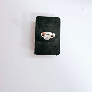 Pode incluir: Um anel de prata com um design simples, apresentado em um fundo preto.