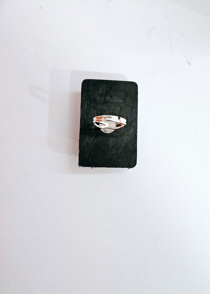 Pode incluir: Um anel de prata com um design simples, apresentado em um fundo preto.