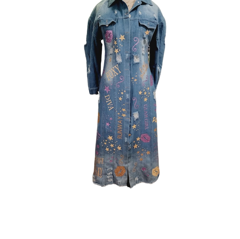 May include: A long denim jacket with a button-up front and long sleeves. The jacket is decorated with gold glitter stars, pink glitter lips, and gold glitter text that says "Runway Diva", "Glams Girl", and "Foxy".