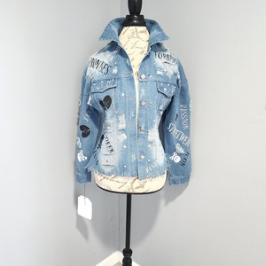 Puede incluir: Una chaqueta vaquera azul claro con detalles desgastados y texto negro que incluye "Forbidden", "Promises", "Broken", "Passion", "Streetwear" y "Icon".