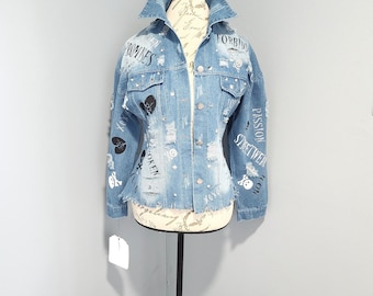 Könnte beinhalten: Eine hellblaue Jeansjacke mit Destroyed-Details und schwarzem Text, darunter "Forbidden", "Promises", "Broken", "Passion", "Streetwear" und "Icon".