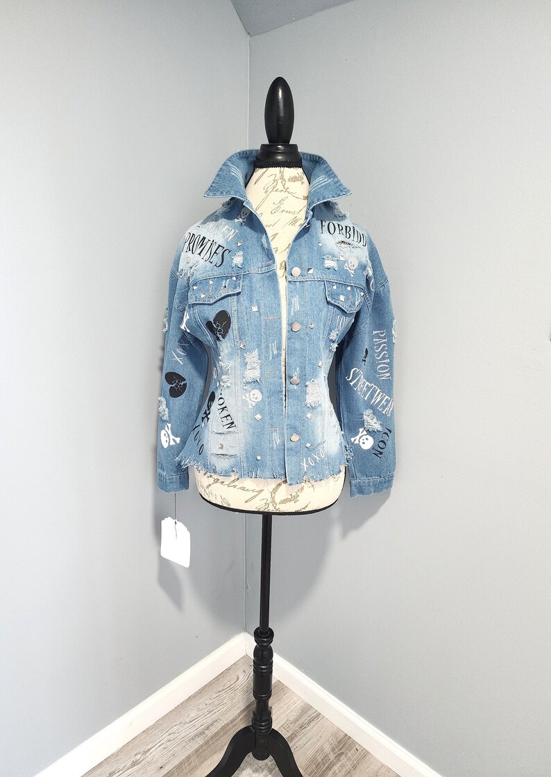 Puede incluir: Una chaqueta vaquera azul claro con detalles desgastados y texto negro que incluye "Forbidden", "Promises", "Broken", "Passion", "Streetwear" y "Icon".