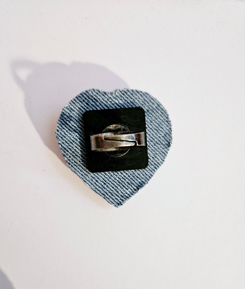 K&ouml;nnte beinhalten: Ein herzf&ouml;rmiger Ring aus Jeans mit einem silbernen Band und einer schwarzen R&uuml;ckseite.