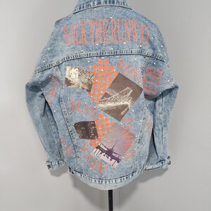 May include: A light blue denim jacket with a patchwork design featuring images of a Ferris wheel, a bridge, a city skyline, and an airplane. The jacket has the text "WALK THE RUNWAY" in orange on the back and is studded with silver rhinestones.
