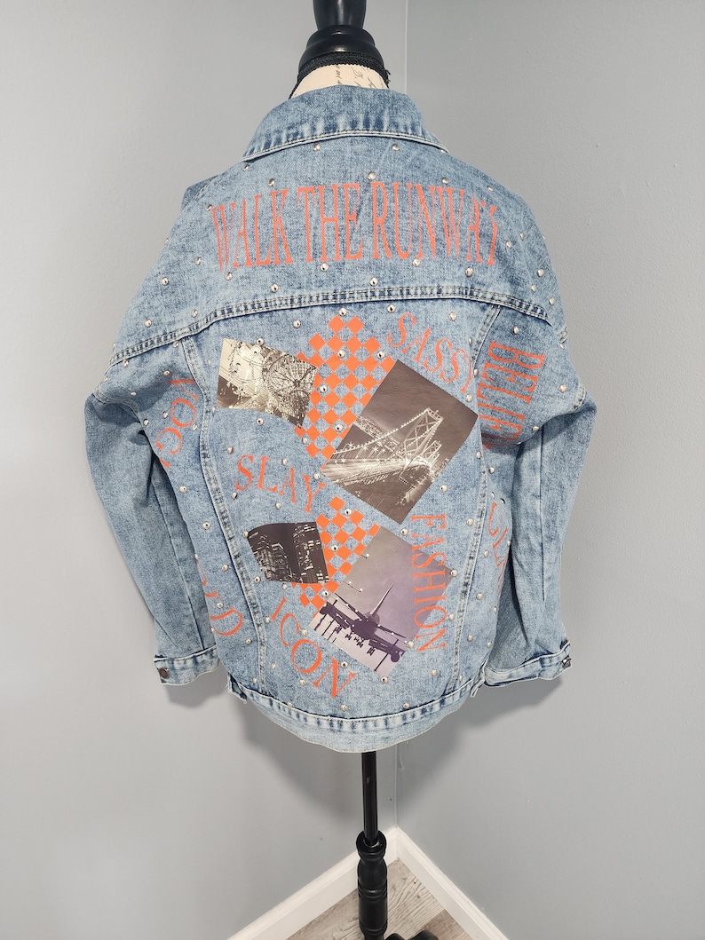 May include: A light blue denim jacket with a patchwork design featuring images of a Ferris wheel, a bridge, a city skyline, and an airplane. The jacket has the text "WALK THE RUNWAY" in orange on the back and is studded with silver rhinestones.