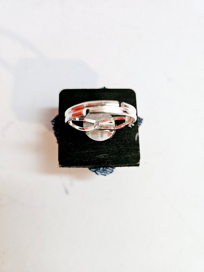 Pode incluir: Um anel de prata com uma pedra redonda e plana de cor prateada engastada no centro. O anel &eacute; apresentado em um fundo preto.