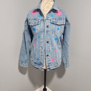 May include: A light blue denim jacket with pink and blue paint splatters.