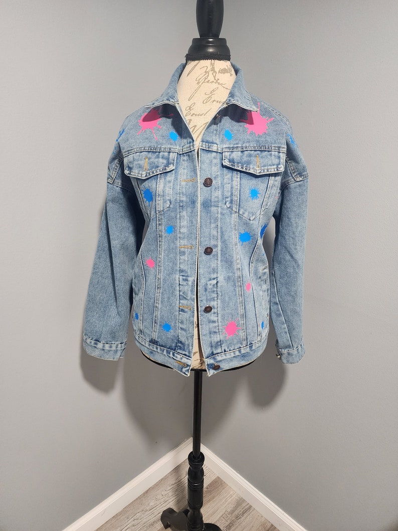 May include: A light blue denim jacket with pink and blue paint splatters.