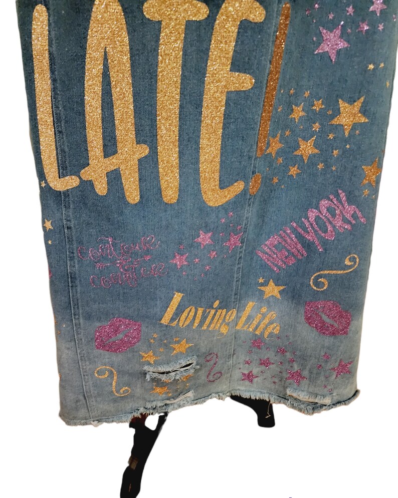 May include: A blue denim jacket with gold glitter lettering that says "LATE!" and "Loving Life" and pink glitter lettering that says "NEW YORK" and has pink glitter stars and lips.