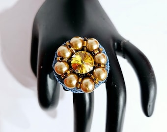 Peut inclure: Une bague en jean avec un gros strass jaune entouré de perles.
