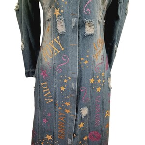 May include: A long denim jacket with distressed details and gold and pink glitter lettering. The lettering includes the words "Foxy Diva", "Runway", "Glam Girl", and "Love You".