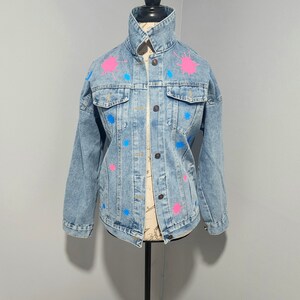 May include: A light blue denim jacket with pink and blue paint splatters.