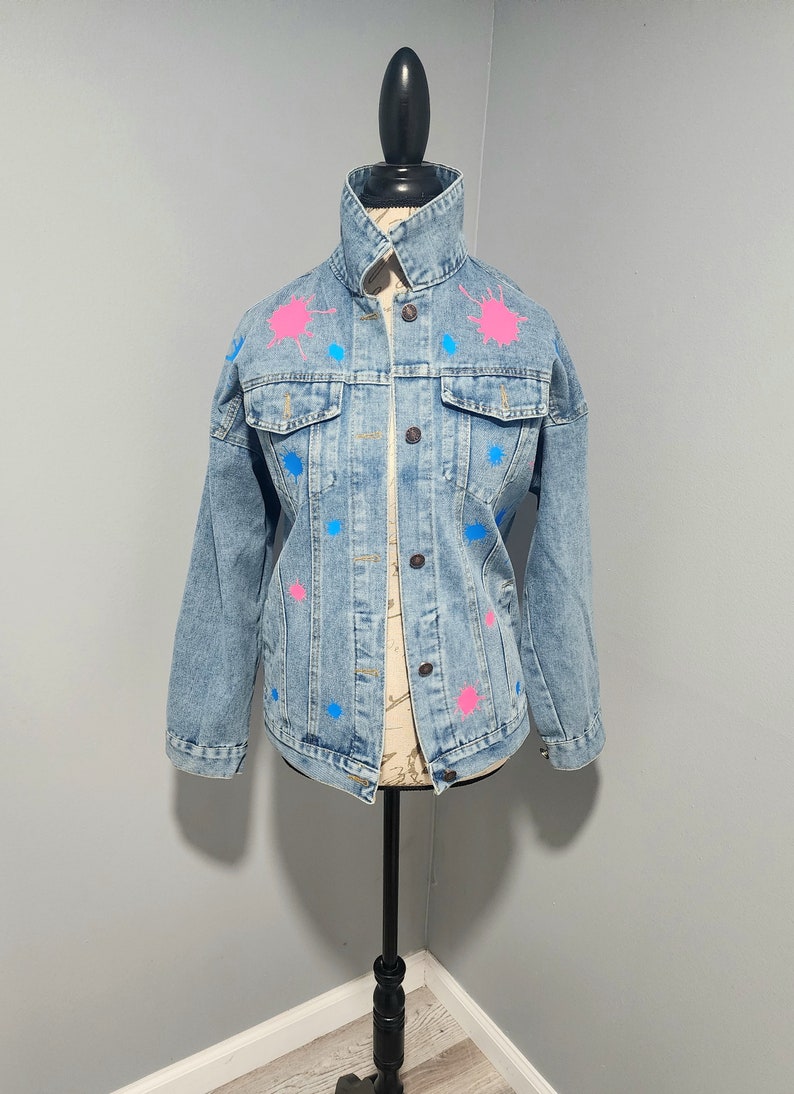 May include: A light blue denim jacket with pink and blue paint splatters.