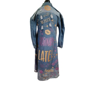 May include: A long denim jacket with distressed details and glitter accents. The jacket features the words "Bossy", "Fashionably Late", "New York", and "Loving Life" in pink and gold glitter.