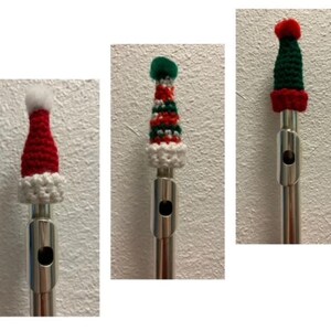 Peut inclure: Trois embouchures de flûte avec des chapeaux de Noël miniatures crochetés. Les chapeaux sont rouges, verts et blancs, avec des pompons et des bordures blanches. Les flûtes sont argentées, sur fond blanc texturé.