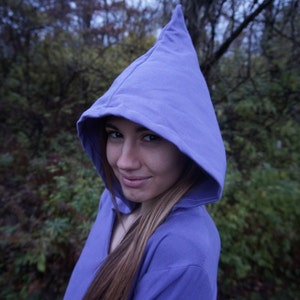 May include: A woman wearing a purple hooded sweatshirt. The hood is pulled up over her head, and she is looking at the camera.