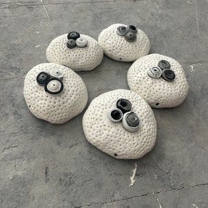 Könnte beinhalten: Fünf weiße Keramik-Kugeln mit einer strukturierten Oberfläche und schwarzen und grauen Papierrosetten auf der Oberseite.