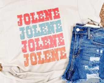 May include: A beige t-shirt with the word "Jolene" repeated four times in a retro font with different colored backgrounds. Each word has small white stars around it.