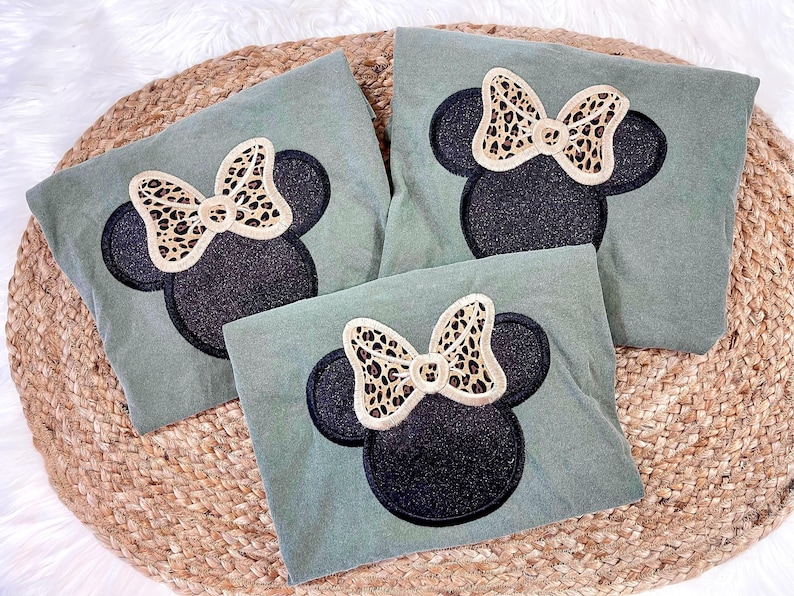 May include: Three green t-shirts with black and gold glitter Mickey Mouse ears and a leopard print bow.