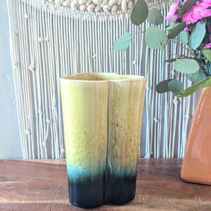Könnte beinhalten: Eine gelbe und blaue Keramikvase in Herzform. Die Vase hat eine gesprenkelte Glasur und einen dunkelblauen Rand.