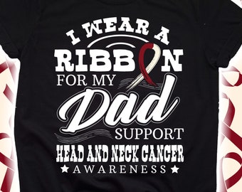 Può includere: Maglietta nera con testo bianco: "I wear a ribbon for my Dad" e un nastro bordeaux. La maglietta dice anche "Support Head and Neck Cancer Awareness" con stelle. È una maglietta a maniche corte e girocollo.