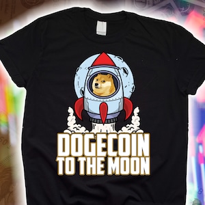 May include: Black t-shirt with a graphic of a Shiba Inu dog in a rocket ship flying to the moon. The text "Dogecoin to the Moon" is printed in gold below the rocket ship.
