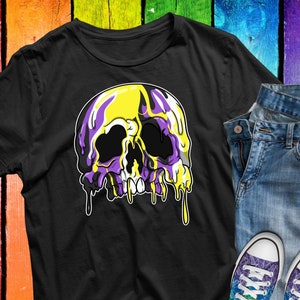 Puede incluir: Camiseta negra con un diseño gráfico de calavera con efecto de pintura goteante amarilla y morada. La imagen también incluye vaqueros azules y un par de zapatillas coloridas con un diseño de arcoíris.