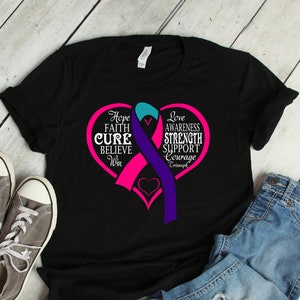 Puede incluir: Camiseta negra con un diseño de corazón rosa y las palabras "Hope, Faith, Cure, Believe, Win" y una cinta turquesa, rosa y morada. La camiseta se muestra con zapatillas grises y vaqueros azules.
