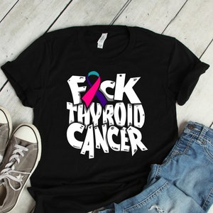 Puede incluir: Camiseta negra con texto blanco que dice "F*CK THYROID CANCER" y una cinta morada, rosa y turquesa.