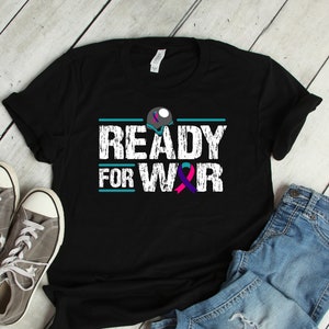 Puede incluir: Camiseta negra con el texto blanco "READY FOR WAR", con una línea turquesa arriba y una cinta turquesa y morada debajo. La camiseta se combina con zapatillas grises y vaqueros azules.