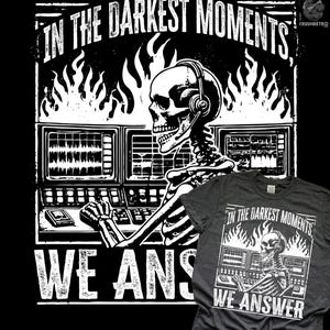 May include: Dark grey t-shirt featuring a white graphic of a skeleton wearing a headset, operating equipment, with flames and the text "IN THE DARKEST MOMENTS, WE ANSWER." The design is a distressed, vintage style.