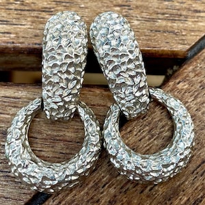 May include: A pair of silver hoop earrings with a textured, hammered finish. The hoops are large and have a circular shape.