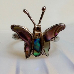 May include: A silver ring with a butterfly design. The butterfly's wings are made of iridescent abalone shell with shades of purple, green, and white.