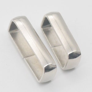 Può includere: Due fermagli per fibbia di cintura in metallo argentato. I fermagli sono rettangolari con bordi arrotondati e una finitura liscia e lucida.