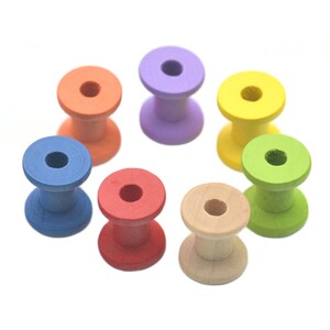 May include: A collection of eight colorful wooden spools in a circular arrangement. The spools are painted in various colors, including orange, purple, yellow, green, blue, red, and natural wood tones. Each spool has a central hole.