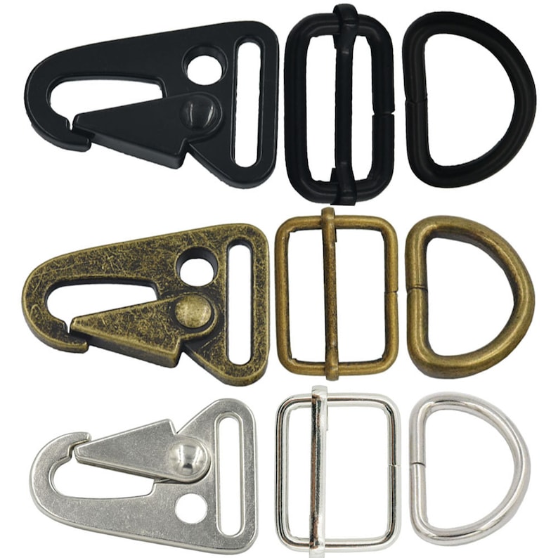 May include: Three sets of metal hardware for attaching straps or leashes. The first set is black, the second is antique gold, and the third is silver. Each set includes a trigger snap, a D-ring, and a slider buckle.