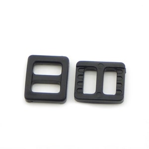 May include: Two black plastic slider buckles. The buckles are rectangular with two holes in the centre. The buckles are used for adjusting the length of straps or belts.
