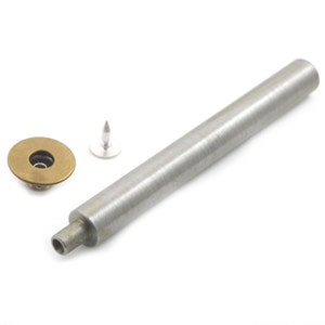 May include: A silver metal tool for setting snaps, with a round brass snap and a silver metal snap stud.