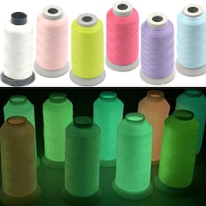 May include: Two rows of spools of thread. The top row has six spools of thread in various colors, including white, pink, yellow, red, purple, and blue. The bottom row has eight spools of thread that glow in the dark, including green, yellow, and orange.