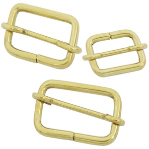 Puede incluir: Tres deslizadores de hebilla de cinturón de metal dorado. Las hebillas son rectangulares con un acabado liso. Las hebillas son de diferentes tamaños.