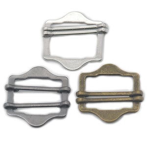 May include: Three metal slider buckles in different finishes: silver, black, and antique gold. Each buckle has a rectangular shape with rounded corners and three parallel bars.