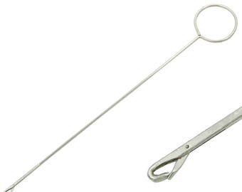 Puede incluir: Un portaagujas quirúrgico de plata con un mango largo y delgado y un bucle circular en el extremo. El portaagujas está diseñado para sujetar y manipular agujas quirúrgicas.