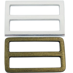 May include: Two metal slider buckles, one silver and one antique brass. Both buckles have a rectangular shape with two parallel slots.
