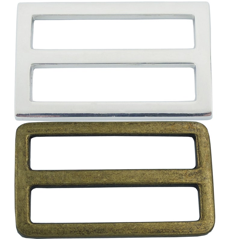 May include: Two metal slider buckles, one silver and one antique brass. Both buckles have a rectangular shape with two parallel slots.