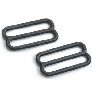 May include: Two black metal slider buckles, each with two oval-shaped loops. These buckles are commonly used for adjusting straps on clothing or accessories.