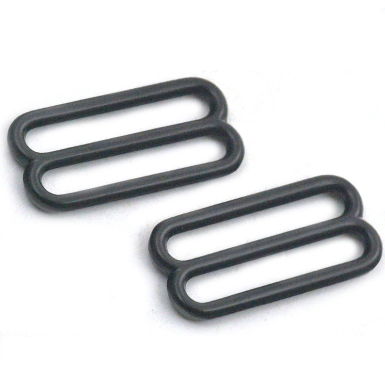 May include: Two black metal slider buckles, each with two oval-shaped loops. These buckles are commonly used for adjusting straps on clothing or accessories.