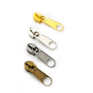 Puede incluir: Cuatro tiradores de cremallera en diferentes acabados: oro, plata, latón antiguo y níquel negro. Cada tirador tiene un bucle en el extremo para sujetarlo a una cremallera.