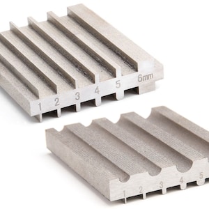 Op de afbeelding: Twee metalen ringmandrels met genummerde groeven voor het bepalen van de ringmaat. De bovenste mandrel heeft zes groeven, genummerd van 1 tot en met 6, en de onderste mandrel heeft vijf groeven, genummerd van 1 tot en met 5. Beide mandrels zijn gemarkeerd met "6 mm".