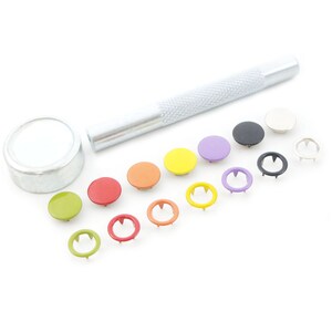 May include: A set of colorful snap fasteners with a tool for attaching them to fabric. The set includes a variety of colors, including red, orange, yellow, green, purple, and black.